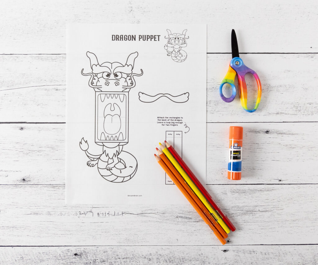 Printable dragon craft printed out. Colored pencils, glue stick, and scissors laying next to it.
