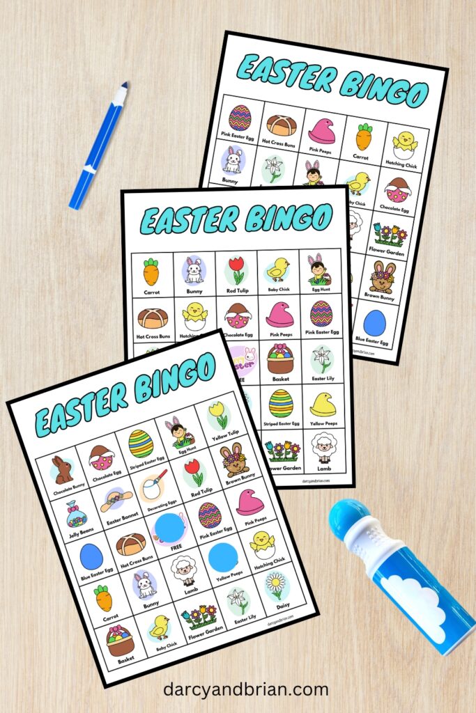 Three different bingo cards for an Easter themed kids game fanned out on a desk. Blue marker and and blue dot marker lay next to them.