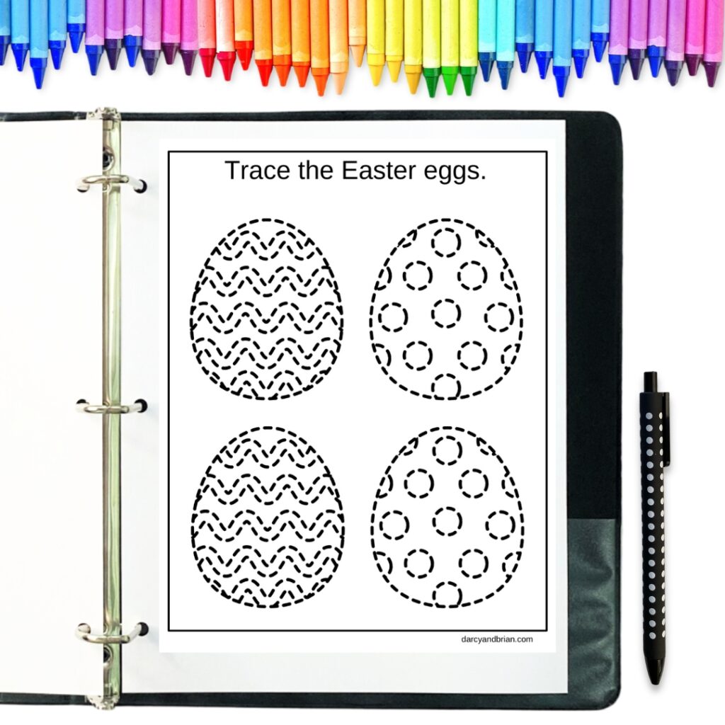 Mockup of one page of Easter eggs with dashed lines for tracing. The paper is in an open binder with a pen next to it. Colorful crayons lined up along the top.