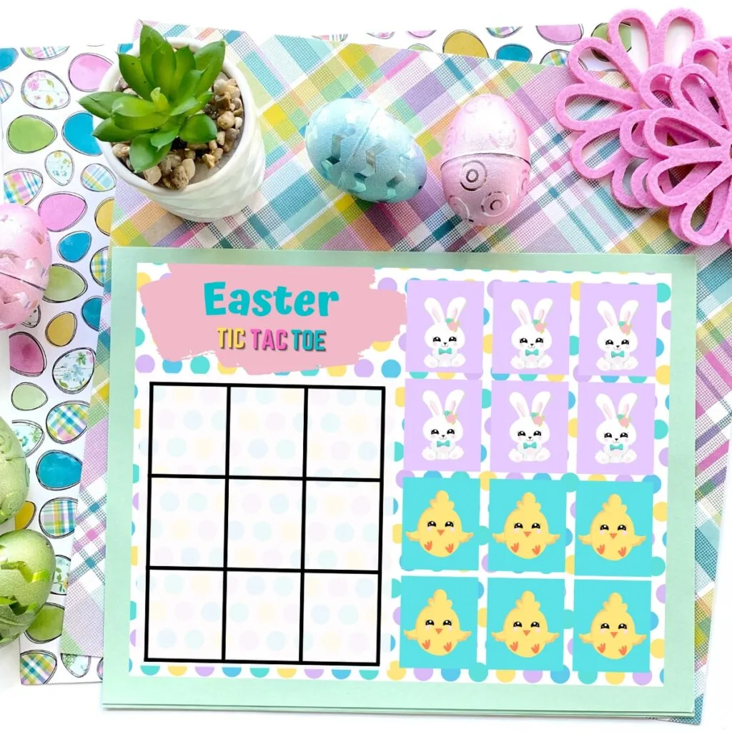 Close up mockup of one colorful Easter tic tac toe printable game board. A small plant and decorative Easter eggs are above it. The tokens are cute chicks and bunnies.