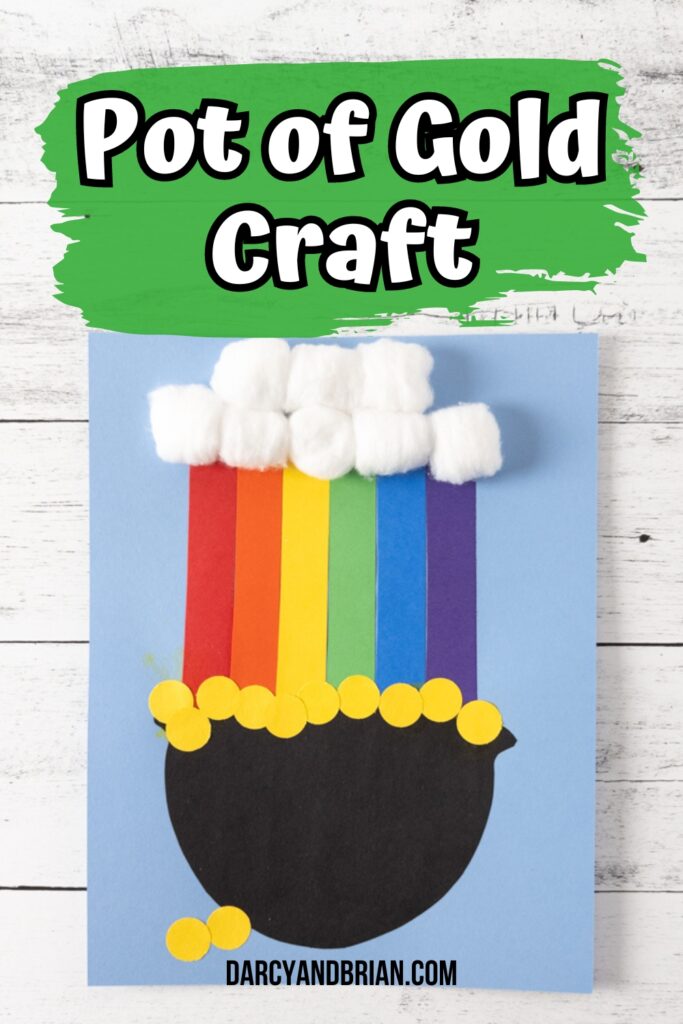 Pot of gold with a rainbow coming out of it made out of construction paper with cotton ball cloud. White text on green brush stroke says Pot of Gold Craft at the top. Project is glued onto a light blue piece of cardstock paper.