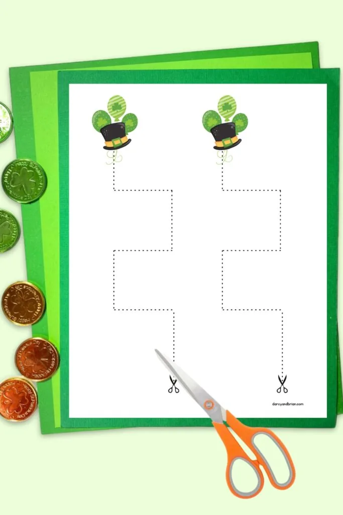 Preview of cutting activity page with leprechaun hats on it laying on top of green papers. Various coins lay along the side and a pair of scissors.