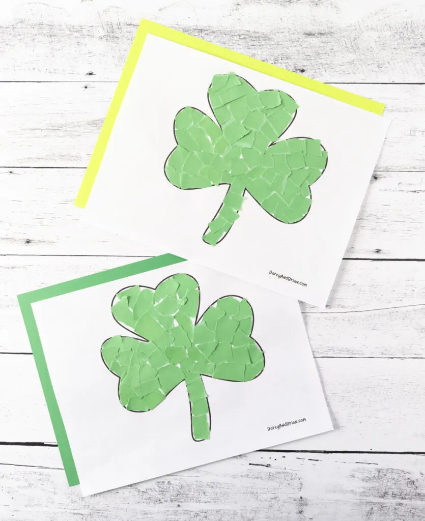 Two completed shamrock crafts made with torn green paper. Each craft template is laying on a piece of colored construction paper. Top one is on yellow and bottom one is on green. 