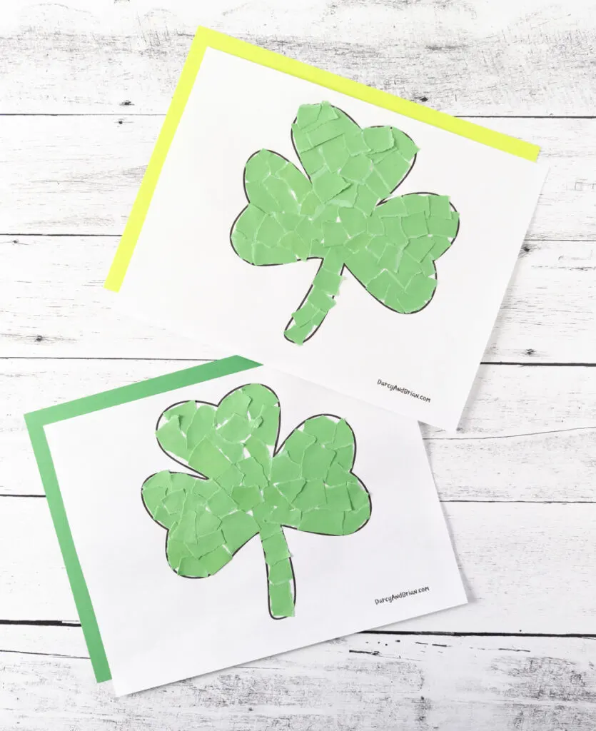 Two completed shamrock crafts made with torn green paper. Each craft template is laying on a piece of colored construction paper. Top one is on yellow and bottom one is on green.