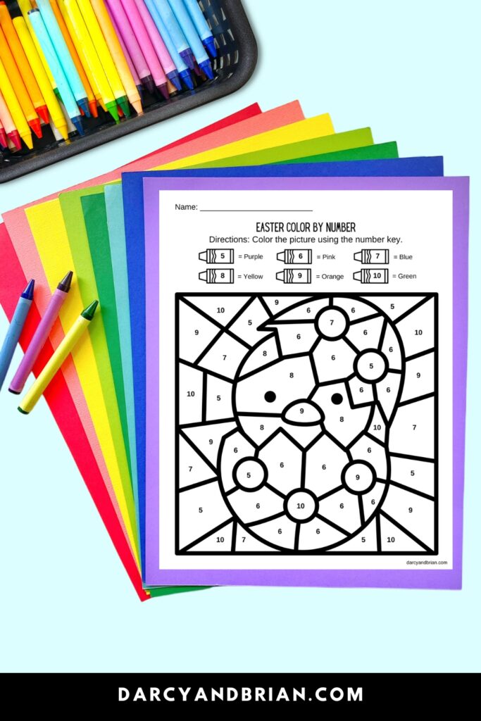 Color by number page with a baby chick hatching. The worksheet is laying on top an assortment of different colored papers. Crayons are in the upper corner.