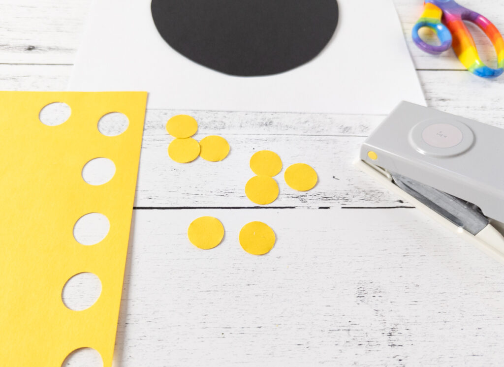 Circle punch on the side next to several yellow circles punched out of construction paper.
