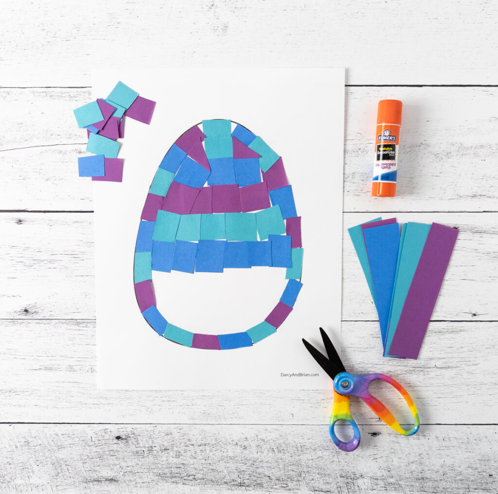 Easter egg craft template with blue and purple paper tiles being glued to cover the template.