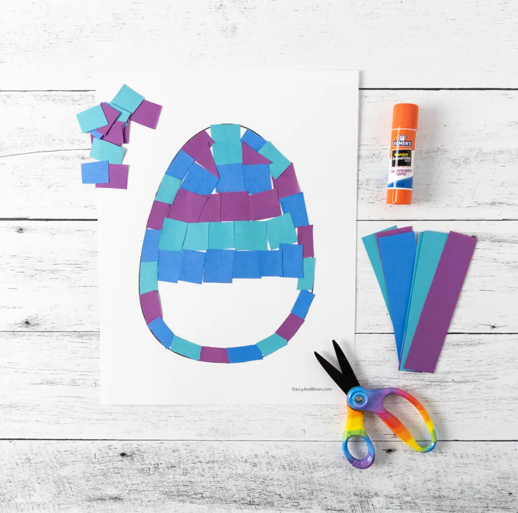 Easter egg craft template with blue and purple paper tiles being glued to cover the template.