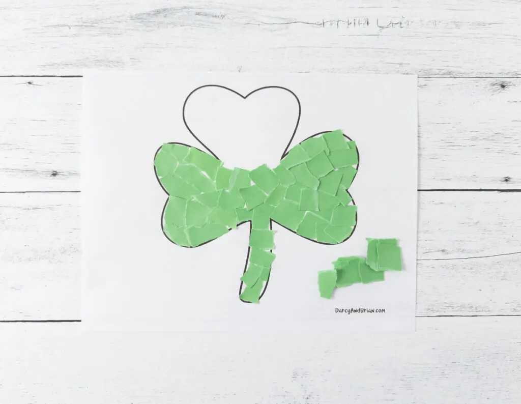 Green pieces of paper glued onto shamrock craft template covering all but the top leaf.