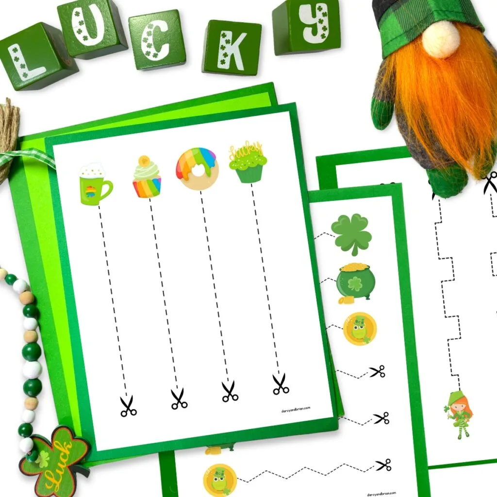 Three Saint Patrick's Day printable cutting practice pages on green papers. Green blocks, beads, and gnome decorate the image around the pages.