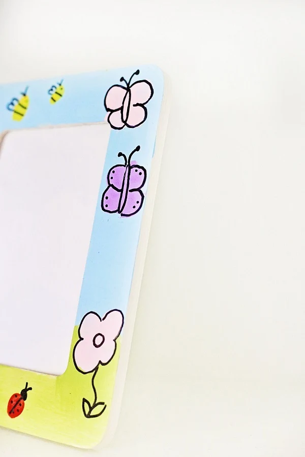 Close up of one side of picture frame with pink and purple fingerprint butterflies and flowers and a red ladybug.