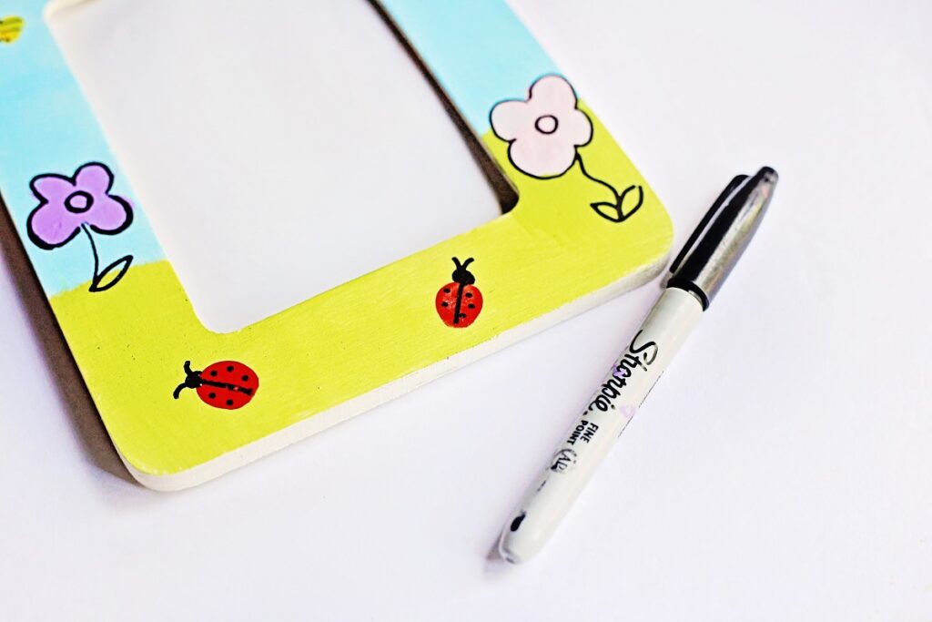 Close up view of fingerprint ladybugs and flowers on painted craft frame with added details using a marker.