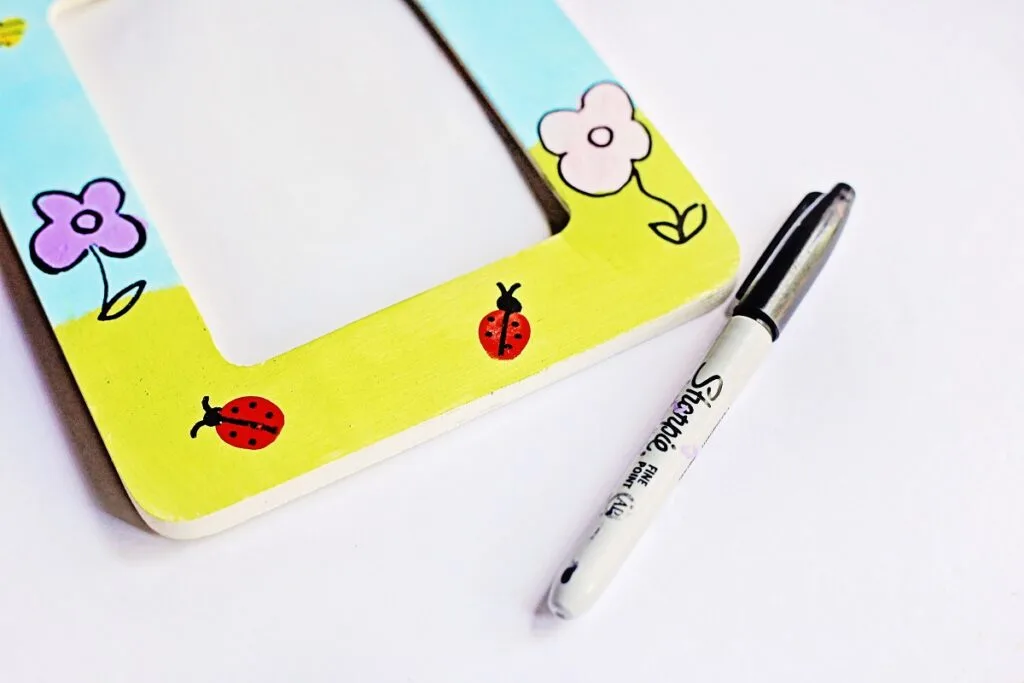 Close up view of fingerprint ladybugs and flowers on painted craft frame with added details using a marker.