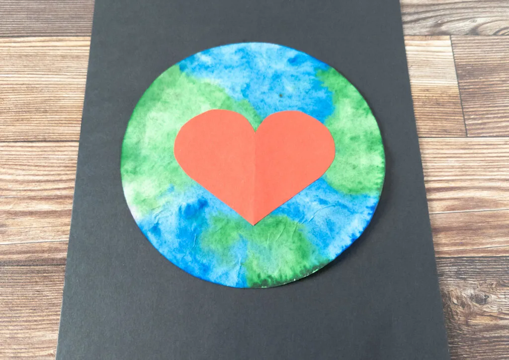 Close up view of completed Earth Day artwork made with a blue and green colored coffee filter and a red construction paper heart in the center.