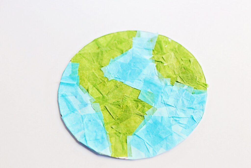 Earth template covered in blue and green tissue paper squares. It is cut out and laying on a white background.