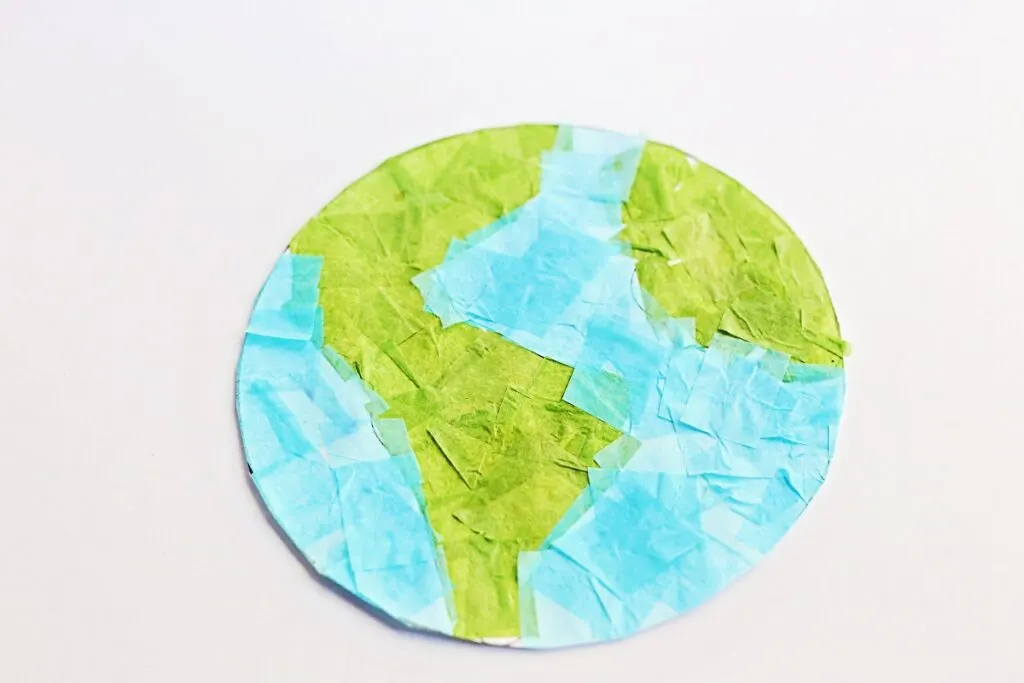 Earth template covered in blue and green tissue paper squares. It is cut out and laying on a white background.