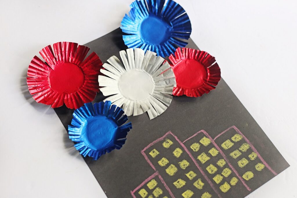 Patriotic colored cupcake liners trimmed and glued to black paper over chalk drawn buildings.