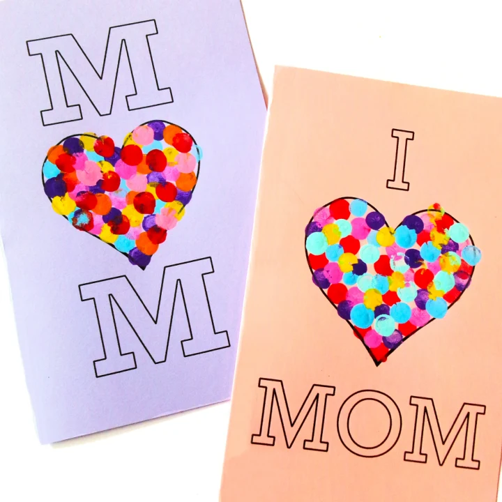 Two finished Mother's Day heart cards decorated with colorful fingerprints. One card on lavender paper says Mom with heart in the center. Pink card says I (heart) Mom.