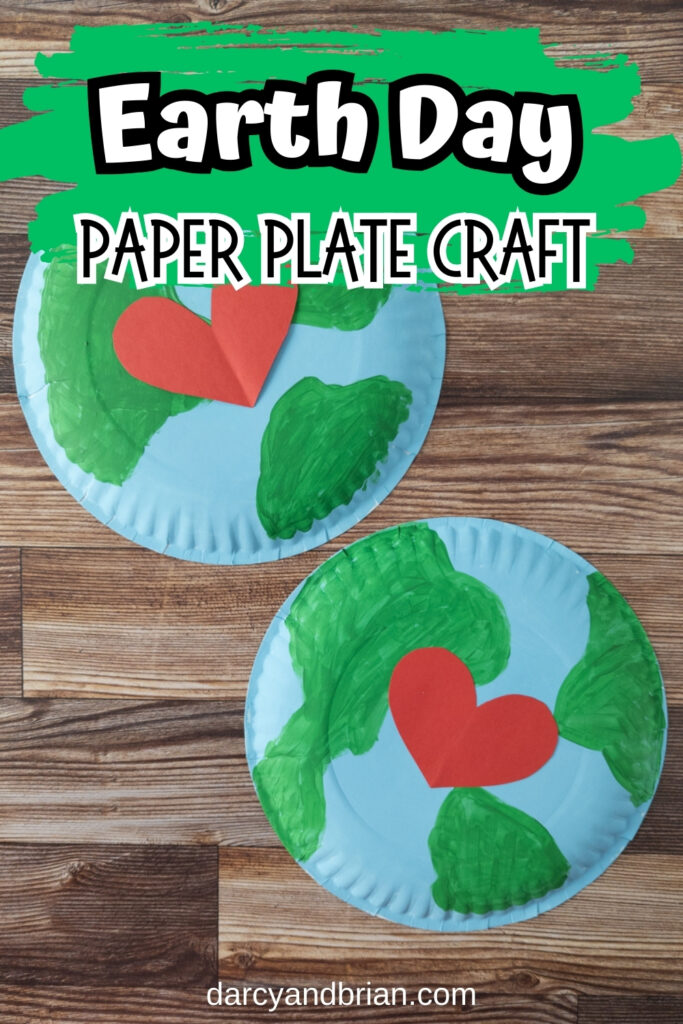 Two large paper plates painted blue and green with red hearts in the middle laying on a wooden table. Top says Earth Day Paper Plate Craft on a green brush stroke background.