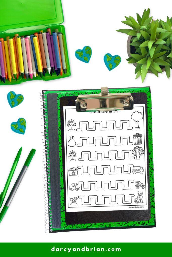 Pencil control worksheet with Earth Day images. Page on clipboard on top of green notebook. Pencil and crayons next to it.