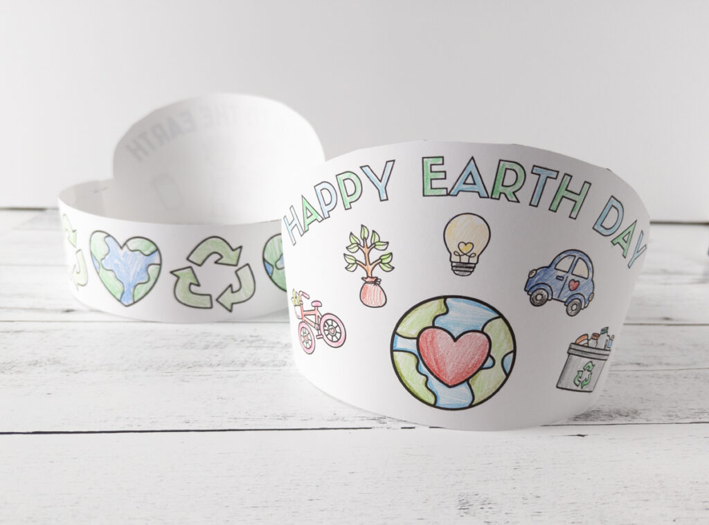 Two completed Earth Day crown headbands. Can see the front of the Happy Earth Day design and the back of the other one, showing the headband strip with heart shaped Earth and recycle sign.