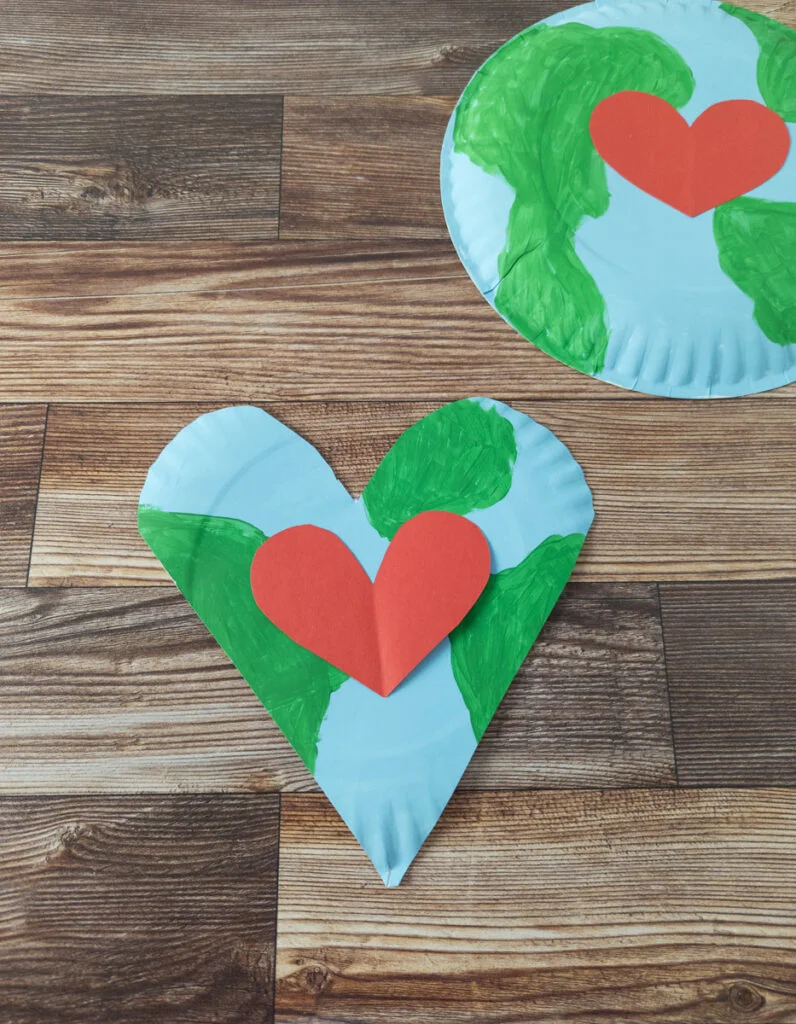 Two plates painted blue and green like the planet Earth. One is cut into heart shape and other is left whole. Both have red paper hearts in the center.
