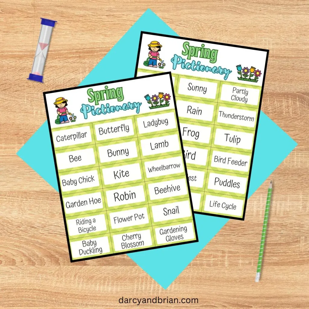 Two pages of spring vocabulary words perfect for drawing prompts overlapping each other on a blue paper on a desk. A green pencil and sand timer nearby.