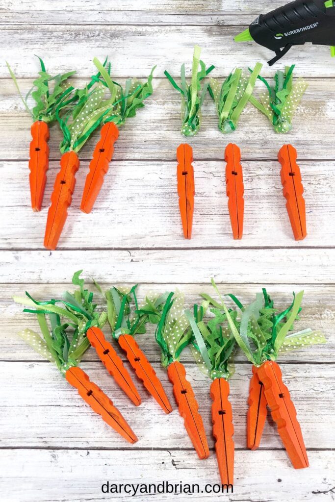 Orange painted clothespins laying near green ribbon bundles and another set with the ribbons glued to the top of the clothespins to look like carrots.