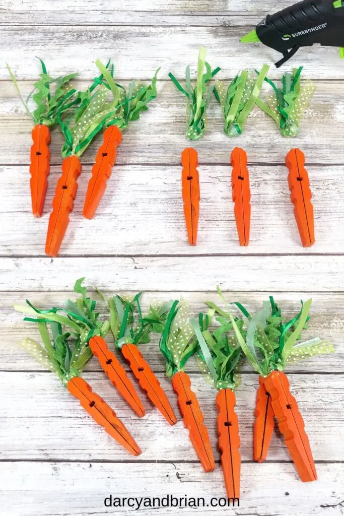 Orange painted clothespins laying near green ribbon bundles and another set with the ribbons glued to the top of the clothespins to look like carrots.