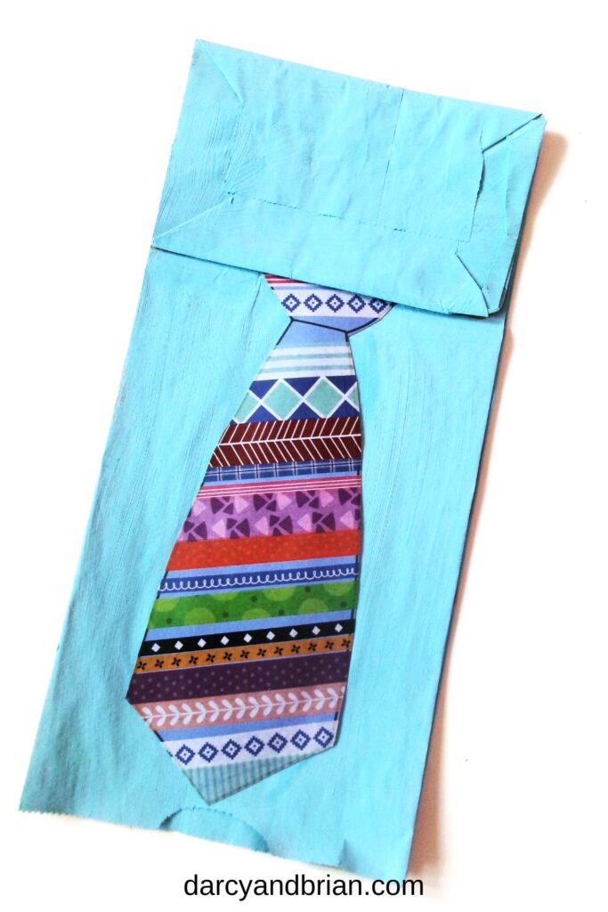 Paper bag painted sky blue to look like a shirt. A washi tape covered paper in a tie shape attached to the bag.