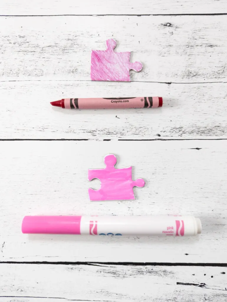 Puzzle piece and crayon used to color it laying near each other. Below them is a pink marker and the puzzle piece colored with the marker.