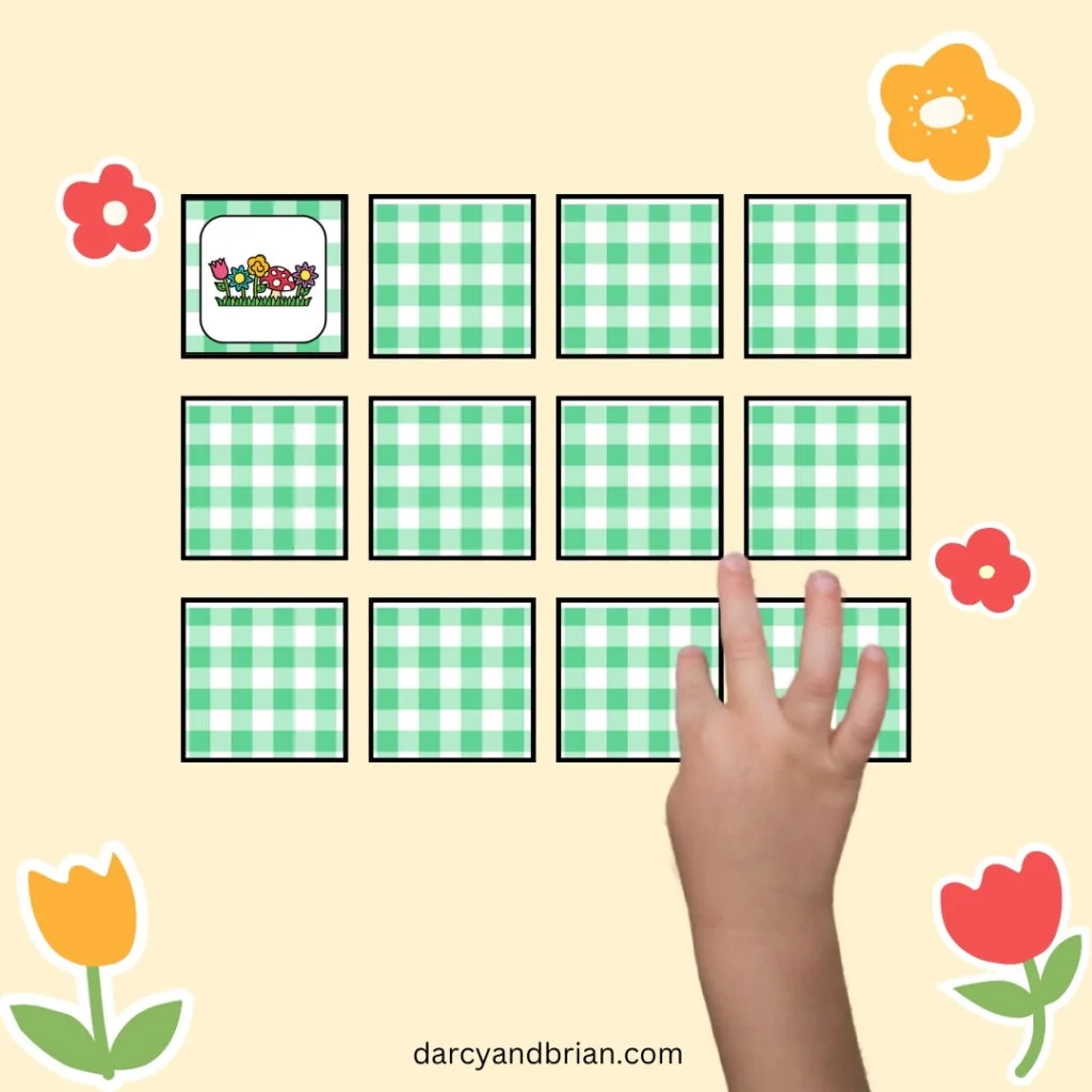12 square game cards arranged in a grid. 11 are face down with green gingham pattern on the back. One card is flipped over showing flowers. A small child's hand is touching another card.