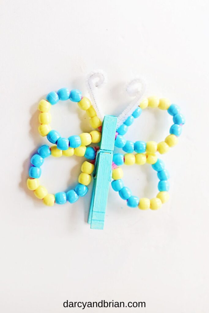 Finished butterfly made with blue painted clothespin and blue and yellow beads on wings.