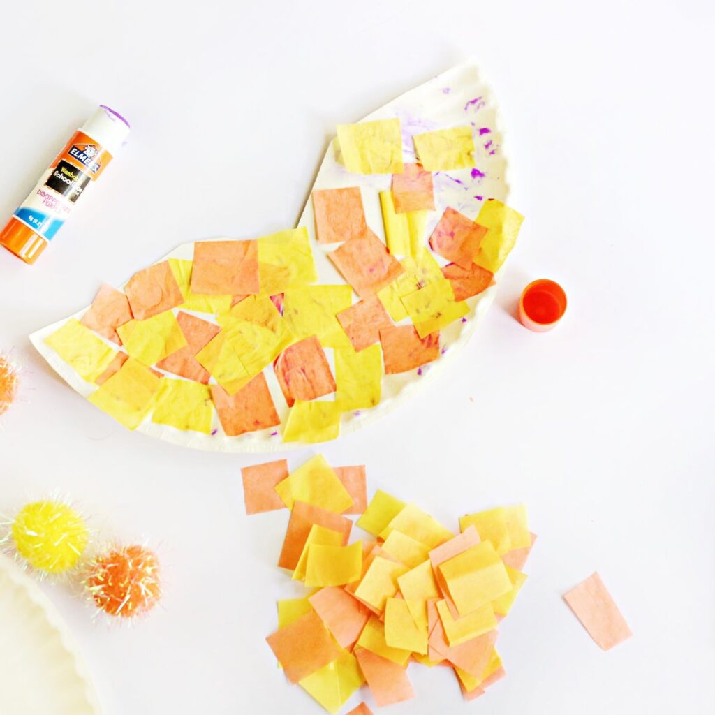 Half of a paper plate covered in yellow and orange tissue paper squares.