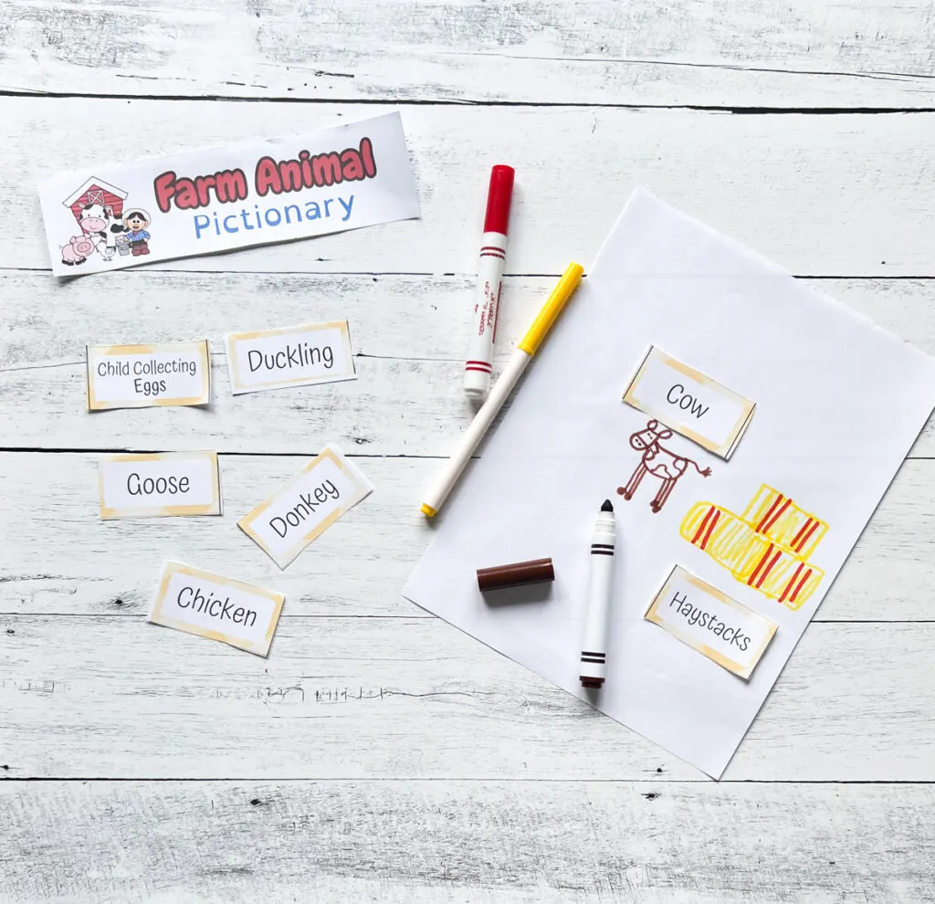 Assorted game cards laying on table beside drawing of a cow and haystacks done with markers.