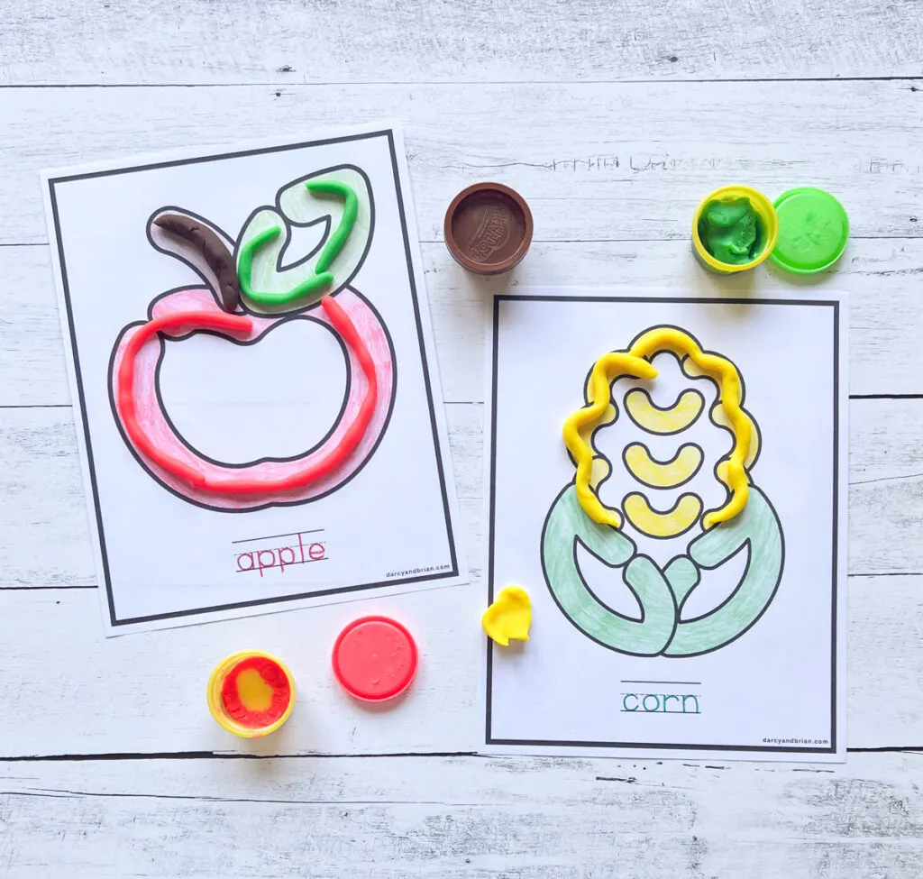 Red and green playdough formed and placed within the lines of the apple mat. Yellow dough added to part of the corn mat.