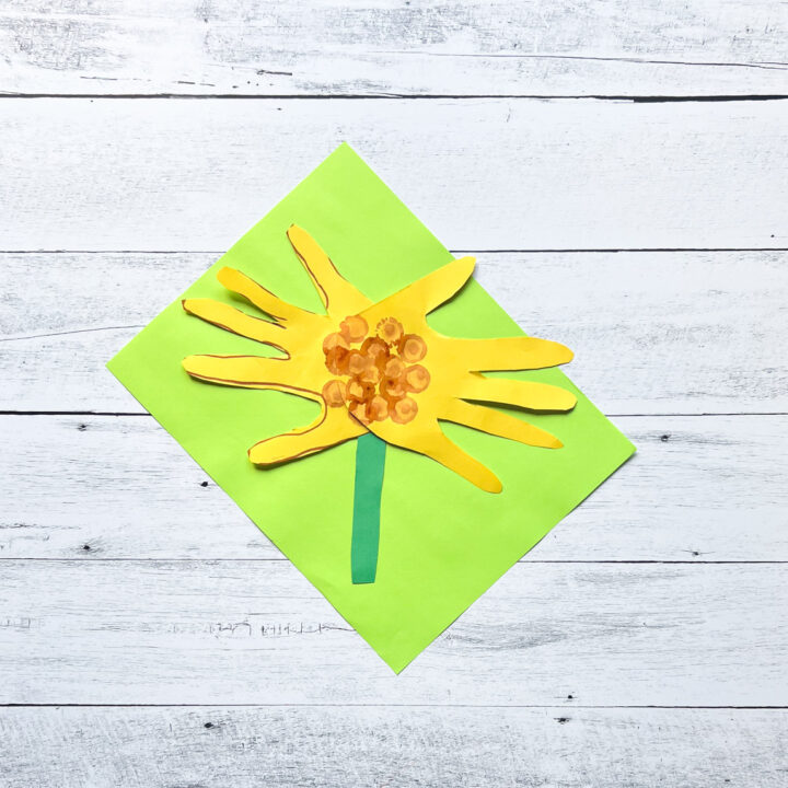 Finished handprint sunflower made out of construction paper laying on top of a bright green paper.