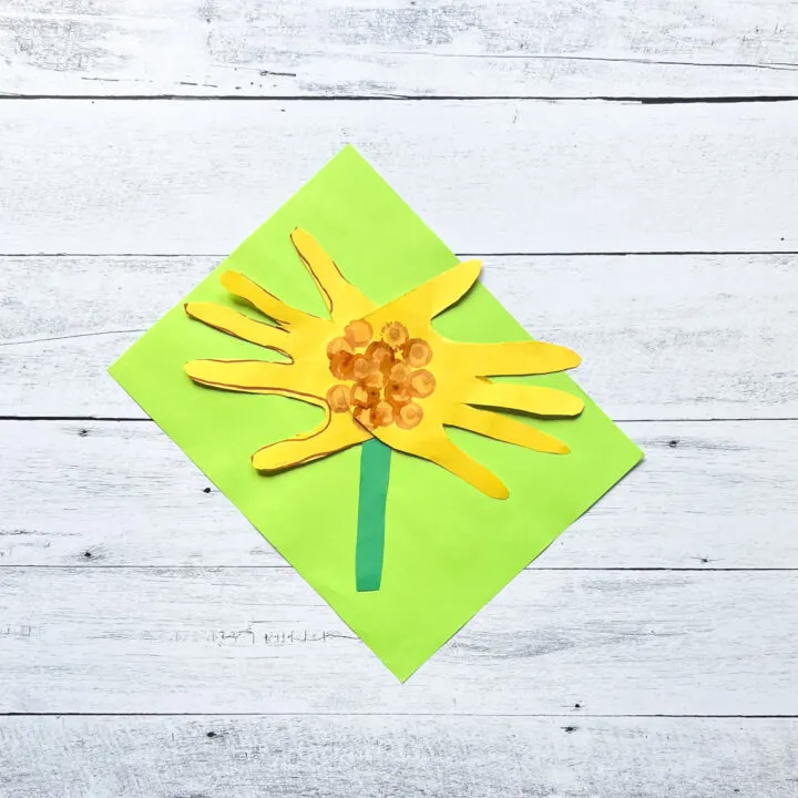 Finished handprint sunflower made out of construction paper laying on top of a bright green paper.