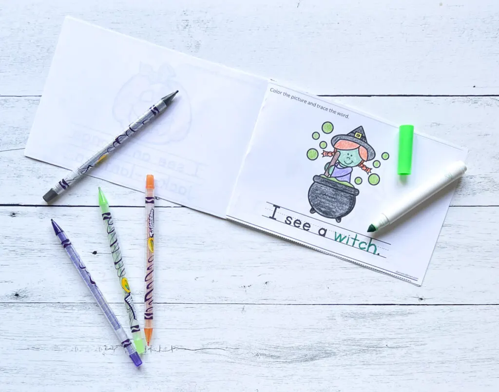 Printable booklet assembled and opened to a page featuring a Halloween witch stirring a cauldron. The picture is colored in, and the sentence "I see a witch" is traced.